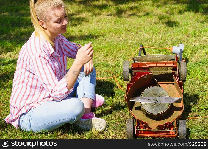 Gardening. Female person gardener mowing green lawn with lawnmower, having problem with broken mower. Female gardener with broken lawnmower