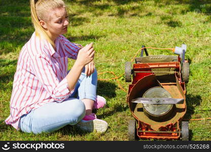 Gardening. Female person gardener mowing green lawn with lawnmower, having problem with broken mower. Female gardener with broken lawnmower