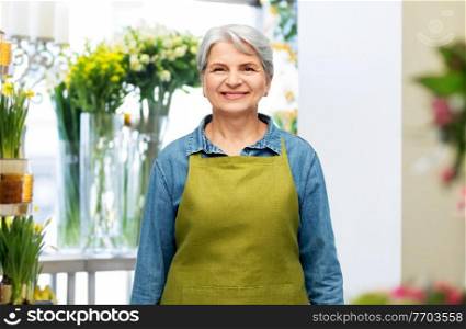 gardening, floristics and old people concept - portrait of smiling senior woman in green garden apron over flower shop background. portrait of smiling senior woman in garden apron