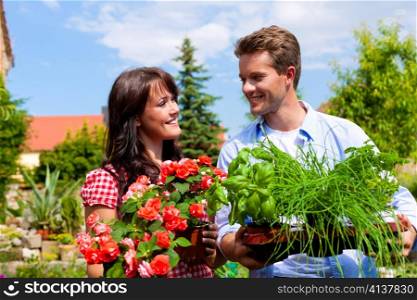 Gardening in summer - happy couple with fresh herbs and red flowers