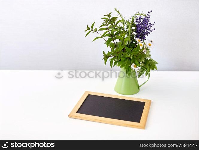 gardening, plants and organic concept - bunch of herbs and flowers in green jug with chalkboard on table. bunch of herbs and flowers with chalkboard