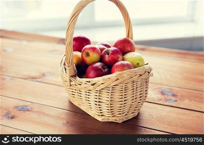 gardening, season, autumn and fruits concept - close up of wicker basket with ripe red apples on wooden table