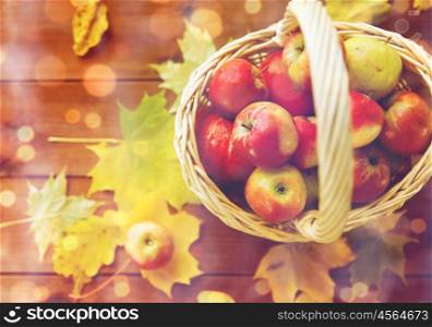 gardening, season, autumn and fruits concept - close up of wicker basket with ripe red apples and leaves on wooden table