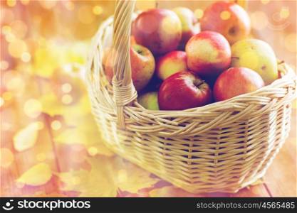 gardening, season, autumn and fruits concept - close up of wicker basket with ripe red apples and leaves on wooden table