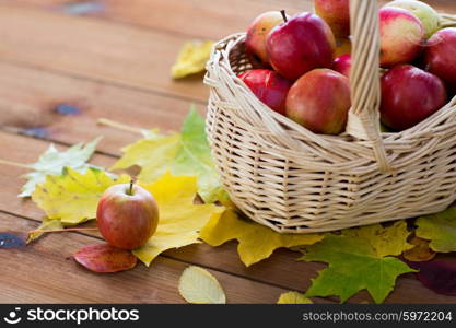 gardening, season, autumn and fruits concept - close up of wicker basket with ripe red apples and leaves on wooden table