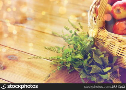 gardening, season, autumn, herbs and fruits concept - close up of wicker basket with ripe red apples and melissa bunch on wooden table