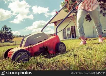 Gardening, taking care of house backyard, agricultural concept. Female person mowing green lawn with lawnmower in sunny day.. Person mowing green grass