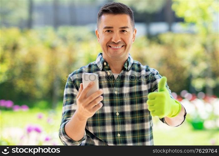 gardening, technology and people concept - happy smiling middle-aged man with smartphone showing thumbs up at summer garden. man with smartphone showing thumbs up at garden