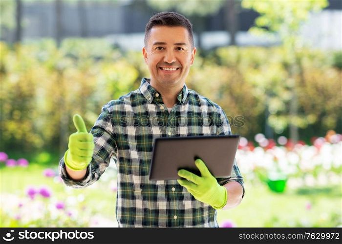 gardening, technology and people concept - happy smiling middle-aged man with tablet pc computer showing thumbs up at summer garden. man with tablet pc showing thumbs up at garden