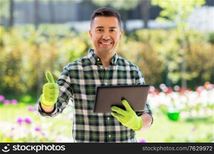 gardening, technology and people concept - happy smiling middle-aged man with tablet pc computer showing thumbs up at summer garden. man with tablet pc showing thumbs up at garden
