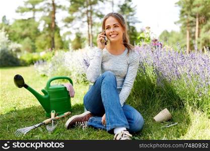 gardening, technology and people concept - happy young woman or gardener with garden tools calling on smartphone in summer. woman calling on smartphone at summer garden