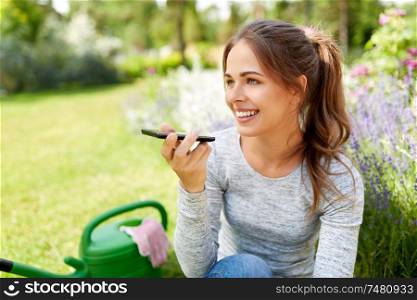 gardening, technology and people concept - happy young woman or gardener with garden tools calling on smartphone or using voice command recorder. gardener recording voice message by smartphone