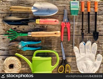Gardening tools and watering can on wooden background flat lay top view.