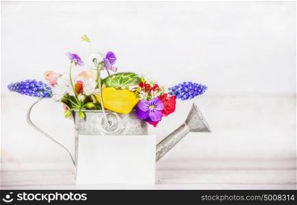 Gardening watering can with garden flowers and greeting card on white wooden background, front view