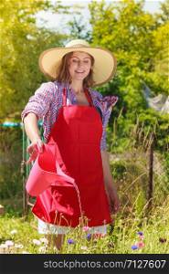 Gardening. Woman in hat red apron working in her backyard garden watering flowers outdoor