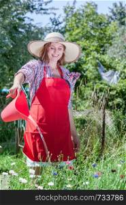 Gardening. Woman in hat red apron working in her backyard garden watering flowers outdoor