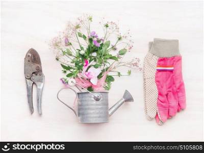 Gardening workspace, garden tools with flowers and watering can on white wooden background, top view, flat lay