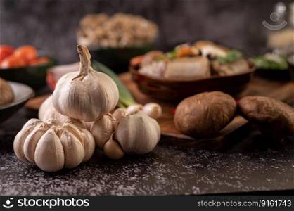 Garlic and shiitake mushrooms are placed on a black cement floor.