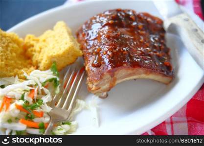 Garlic barbecue sauce on baby back ribs with cornbread and coleslaw on white platter