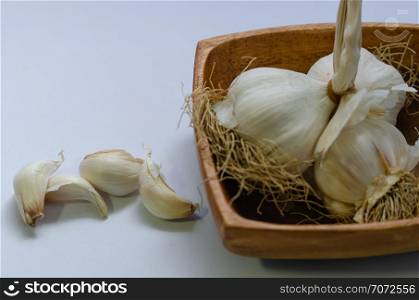 Garlic bulbs in wooden bowl on white background. Pile of garlic on table.