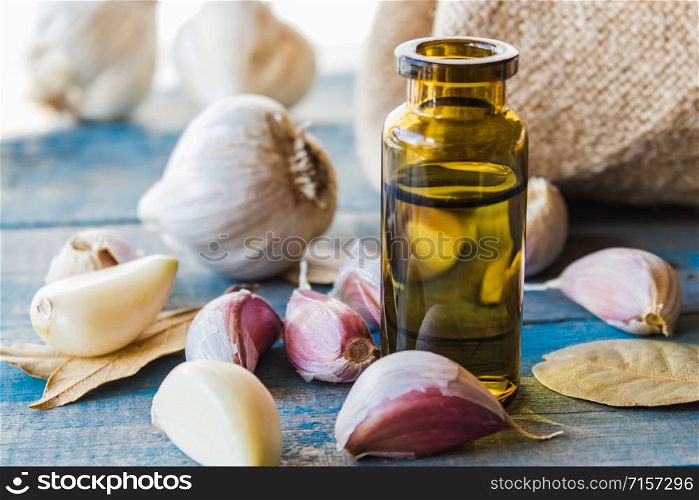 Garlic essential oil in a glass bottle near ripe garlic on a background of blue old wooden boards. Cure or seasoning with garlic.. Garlic essential oil in a glass bottle near ripe garlic on a background of blue old wooden boards.