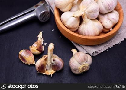 garlic in a wooden bowl and on a black table, top view