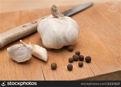 Garlic, kitchen knife and allspice on chopping board