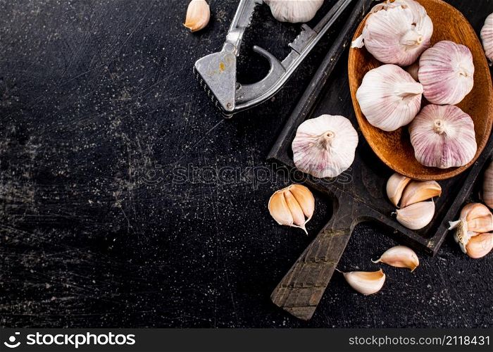 Garlic on a wooden plate on a cutting board. On a black background. High quality photo. Garlic on a wooden plate on a cutting board.