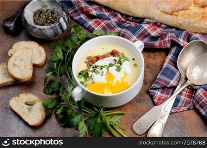 Garlic potato cream soup with bacon and poached eggs, herbs, spices
