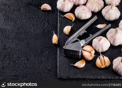 Garlic with a garlic press on a stone board. On a black background. High quality photo. Garlic with a garlic press on a stone board.