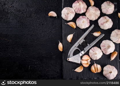 Garlic with a garlic press on a stone board. On a black background. High quality photo. Garlic with a garlic press on a stone board.