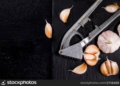 Garlic with a garlic press on a stone board. On a black background. High quality photo. Garlic with a garlic press on a stone board.