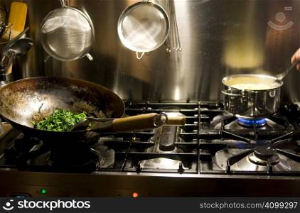 Gasoven with wok and spinach and small pan on fire