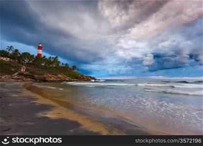 Gathering storm on beach and Kovalam (Vizhinjam) lighthouse on stormy sunset. Kerala, India