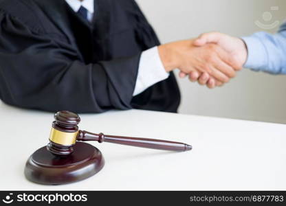 Gavel Justice hammer on wooden table with judge and client shaking hands after adviced in background at courtroom, lawyer service concept