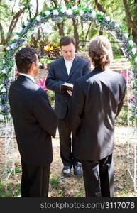 Gay couple being married by their minister outdoors under a floral archway.