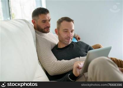 Gay couple consulting their travel plans together with a digital tablet. Homosexual Lifestyle concept.. Gay couple consulting their travel plans together with a digital tablet.