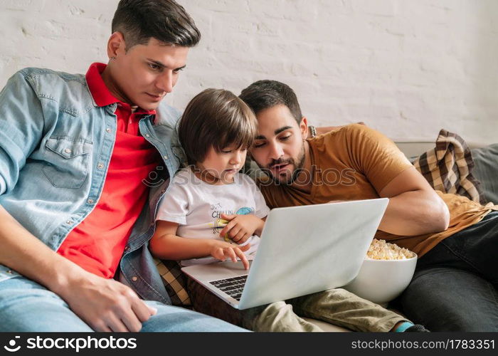 Gay couple enjoying time with their son while watching a movie together on the sofa at home. Family concept.