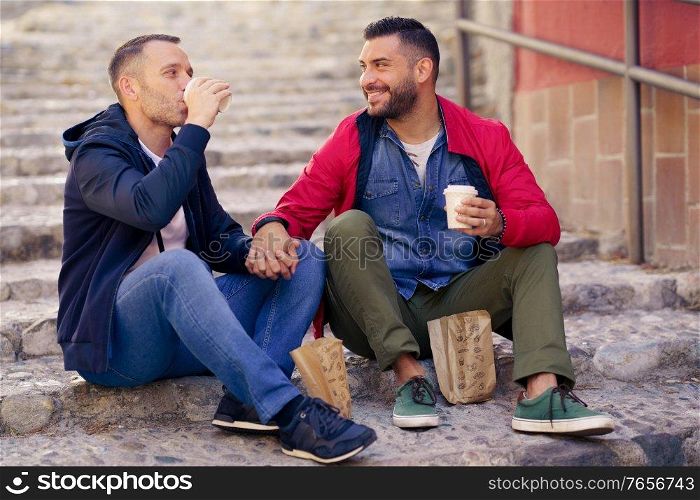 Gay couple having a take-away meal on the street. Homosexual relationship concept.. Gay couple having a take-away meal on the street