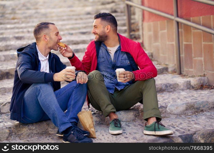 Gay couple having a take-away meal on the street. Homosexual relationship concept.. Gay couple having a take-away meal on the street