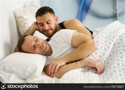 Gay couple hugging on their bed. Homosexual lifestyle concept.. Gay couple hugging on their bed at home.