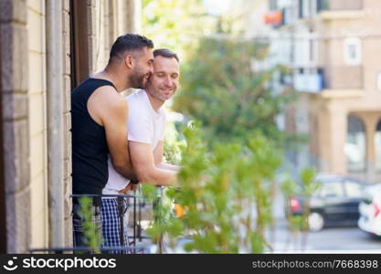 Gay couple in a romantic moment leaning out of their balcony. Homosexual lifestyle concept.. Gay couple in a romantic moment leaning out of their balcony.