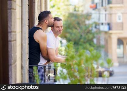 Gay couple in a romantic moment leaning out of their balcony. Homosexual lifestyle concept.. Gay couple in a romantic moment leaning out of their balcony.