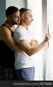 Gay couple in a romantic moment near a window. Homosexual lifestyle concept.. Gay couple in a romantic moment near a window.