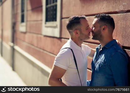 Gay couple kissing outdoors in urban background. Homosexual relationship concept.. Gay couple kissing outdoors in urban background.
