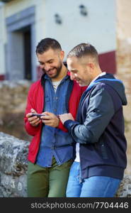 Gay couple looking at their smartphone. Homosexual relationship concept.. Gay couple looking at their smartphone outdoors