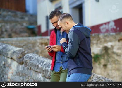 Gay couple looking at their smartphone. Homosexual relationship concept.. Gay couple looking at their smartphone outdoors