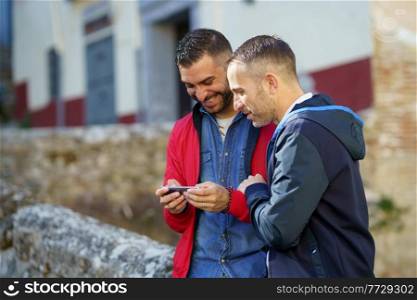 Gay couple looking at their smartphone. LGTB relationship concept.. Gay couple looking at their smartphone outdoors