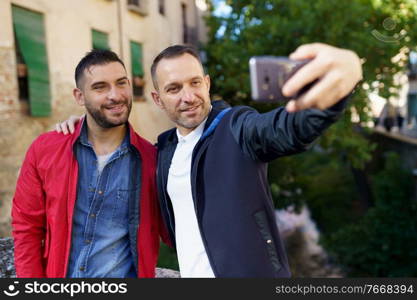 Gay couple making a selfie with their smartphone. Homosexual relationship concept.. Gay couple making a selfie with their smartphone.