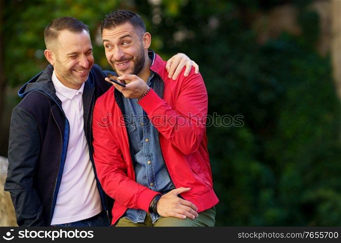 Gay couple recording a voice note together on their smartphone. Homosexual relationship concept.. Gay couple recording a voice note together on their smartphone.